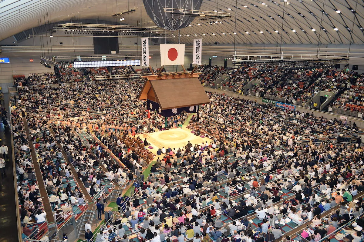 A tourist challenging a sumo wrestler in the dohyo ring at a live sumo show in Osaka, Japan